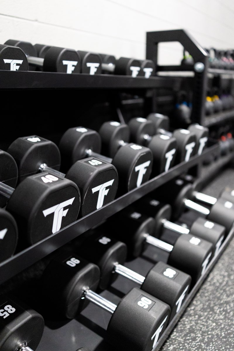 Racks of Triple F branded dumbbells along the weight room wall.
